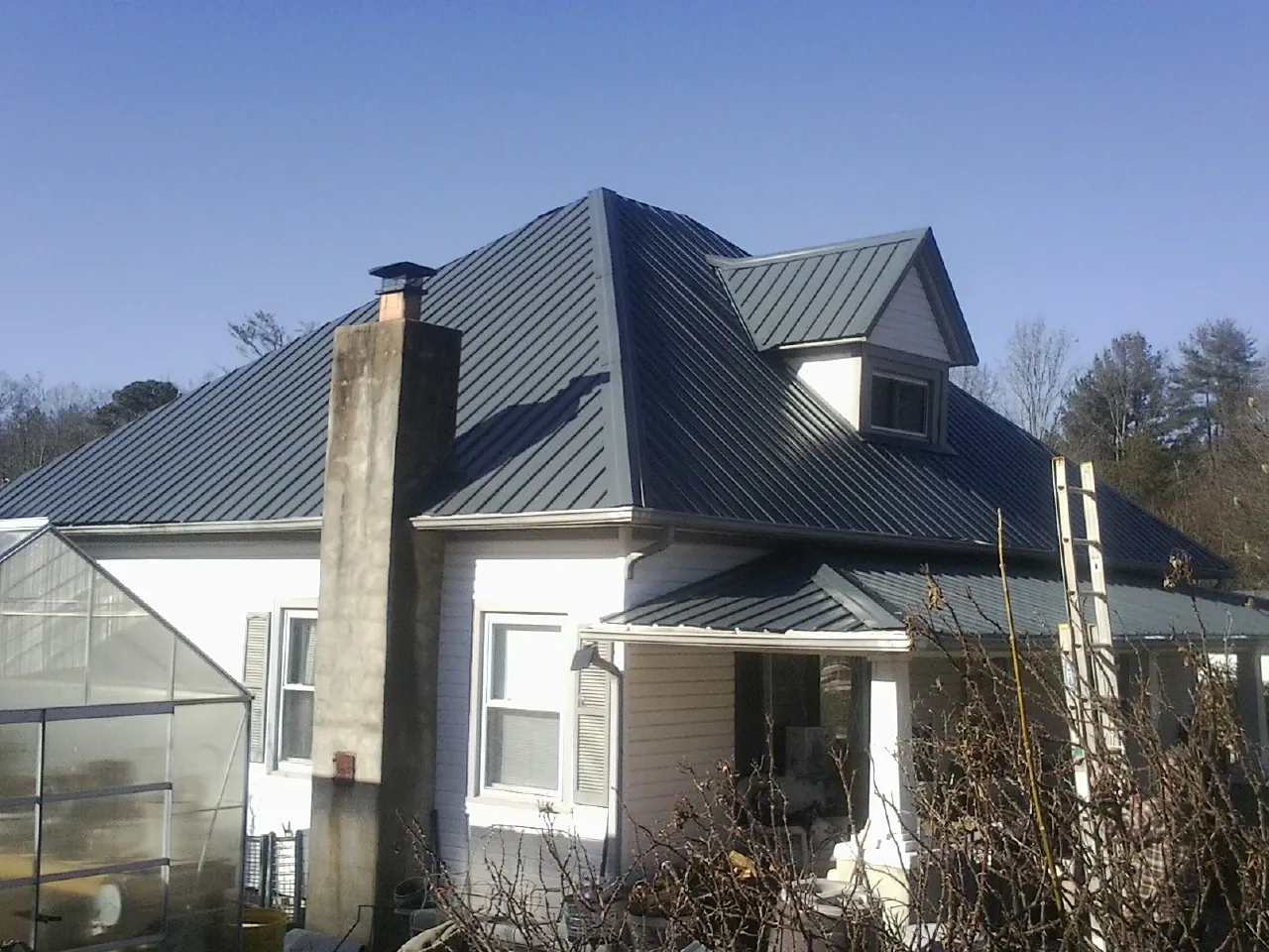 Dark blue standing seam metal roof on a white farmhouse with dormer — Slate & Tile Roof Repair by Roofing Brothers in Fitzgerald