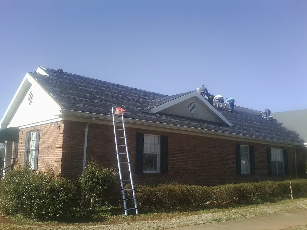 Crew tearing shingles off a brick ranch roof with a ladder set — Emergency Roof Repair work by our crew in Fitzgerald