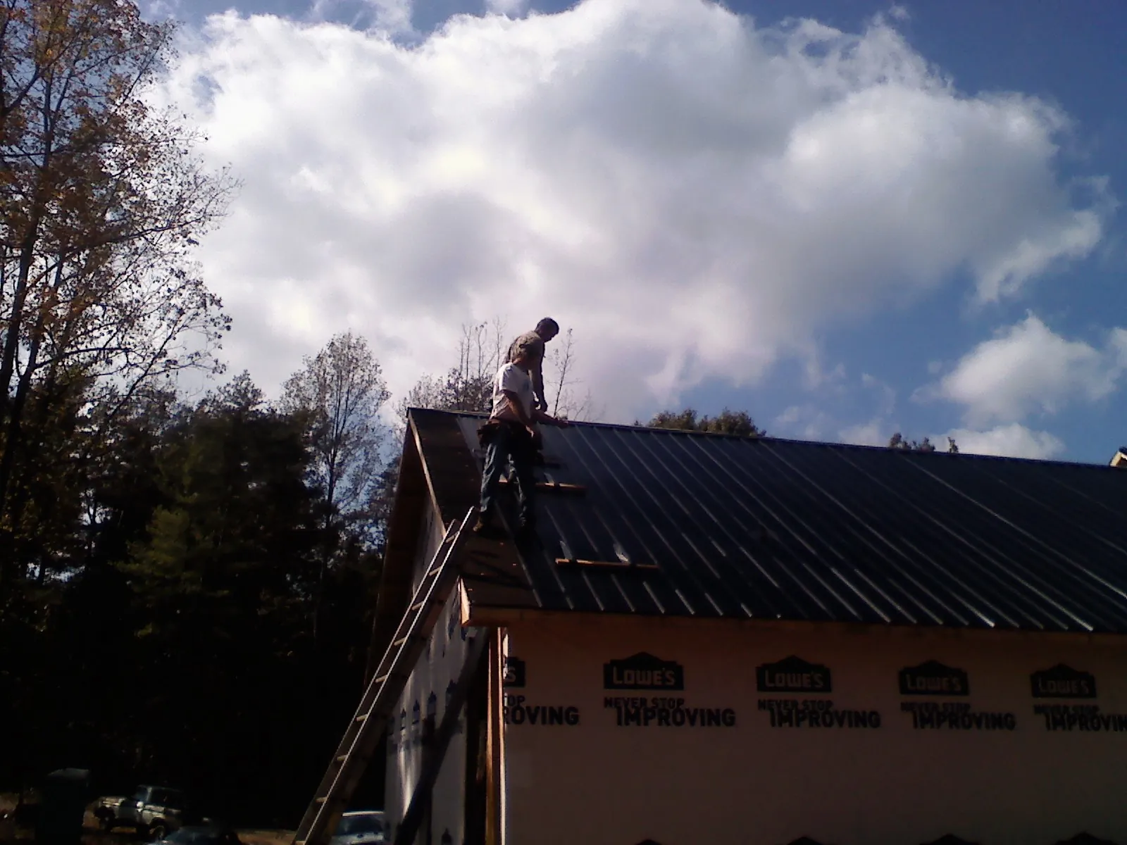 Roofer fastening dark metal panels high against a cloudy sky, from a Roof Inspection job in Fitzgerald